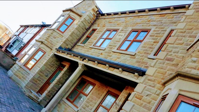 A new-build house in coursed sandstone with a bay window and stone porch