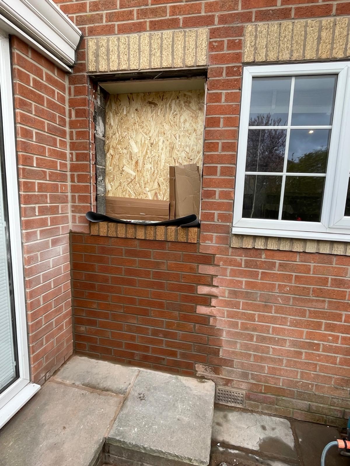 A brick wall being altered around a boarded window opening