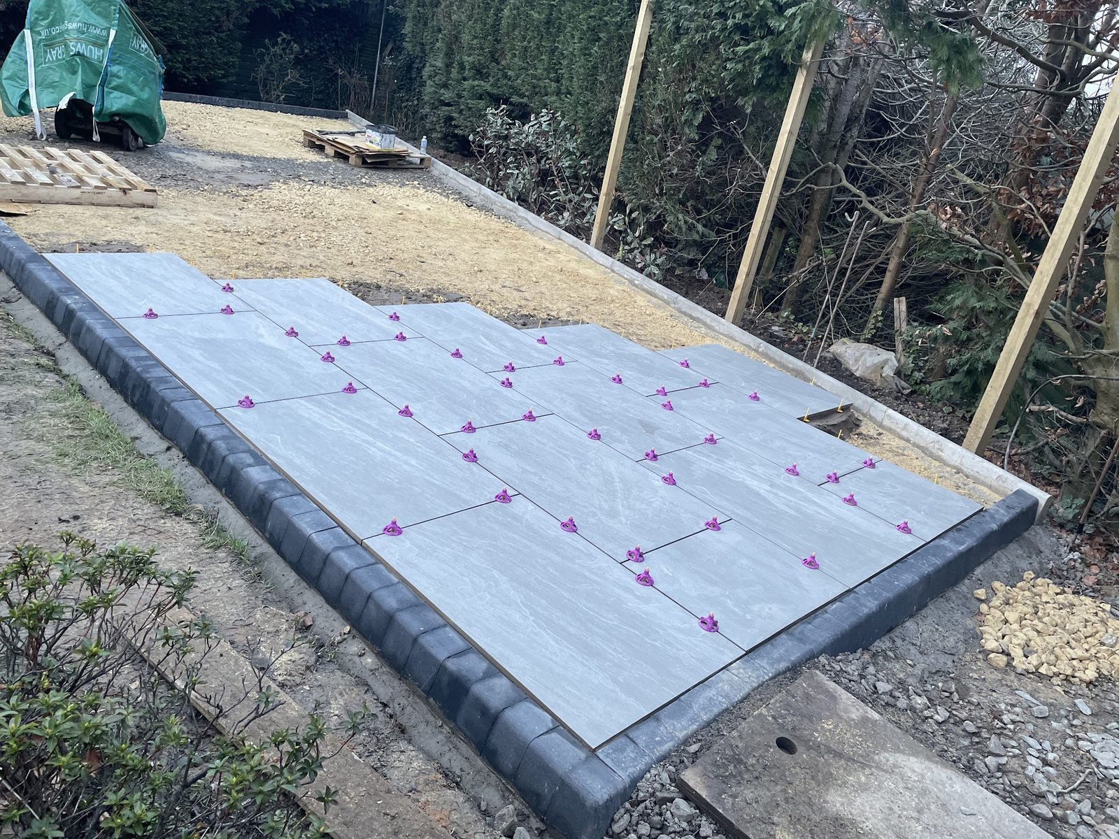 Grey patio slabs being laid with spacers inside a kerb edge