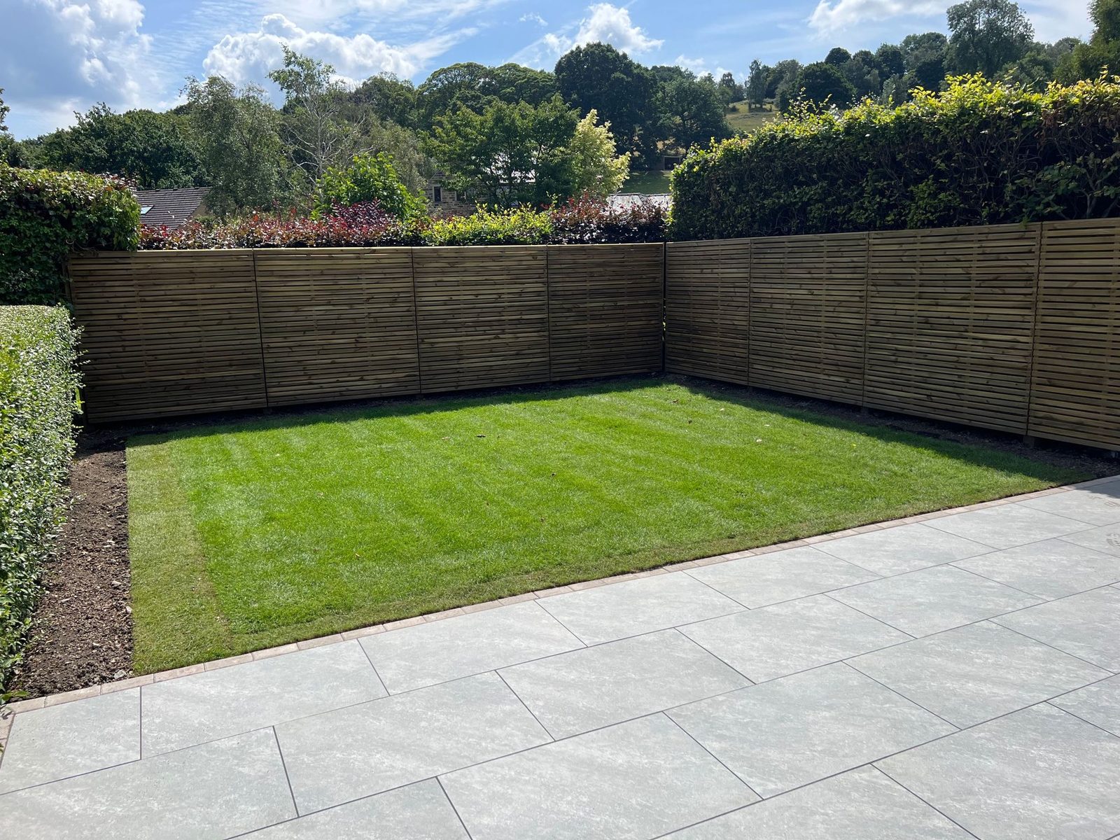 A finished garden with a new lawn, a grey porcelain patio and a slatted fence